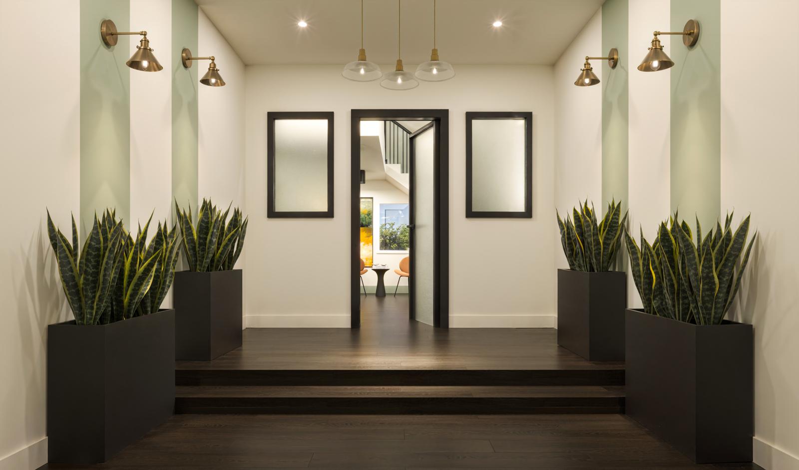 Symmetrical entry vestibule with sage stripes, brass sconces and planted black troughs