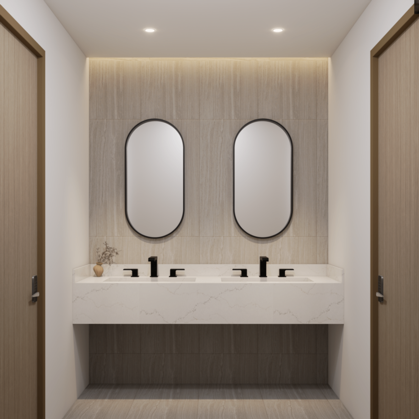 Office restroom vanity with two arched black-framed mirrors, pale stone wall and integrated cove lighting